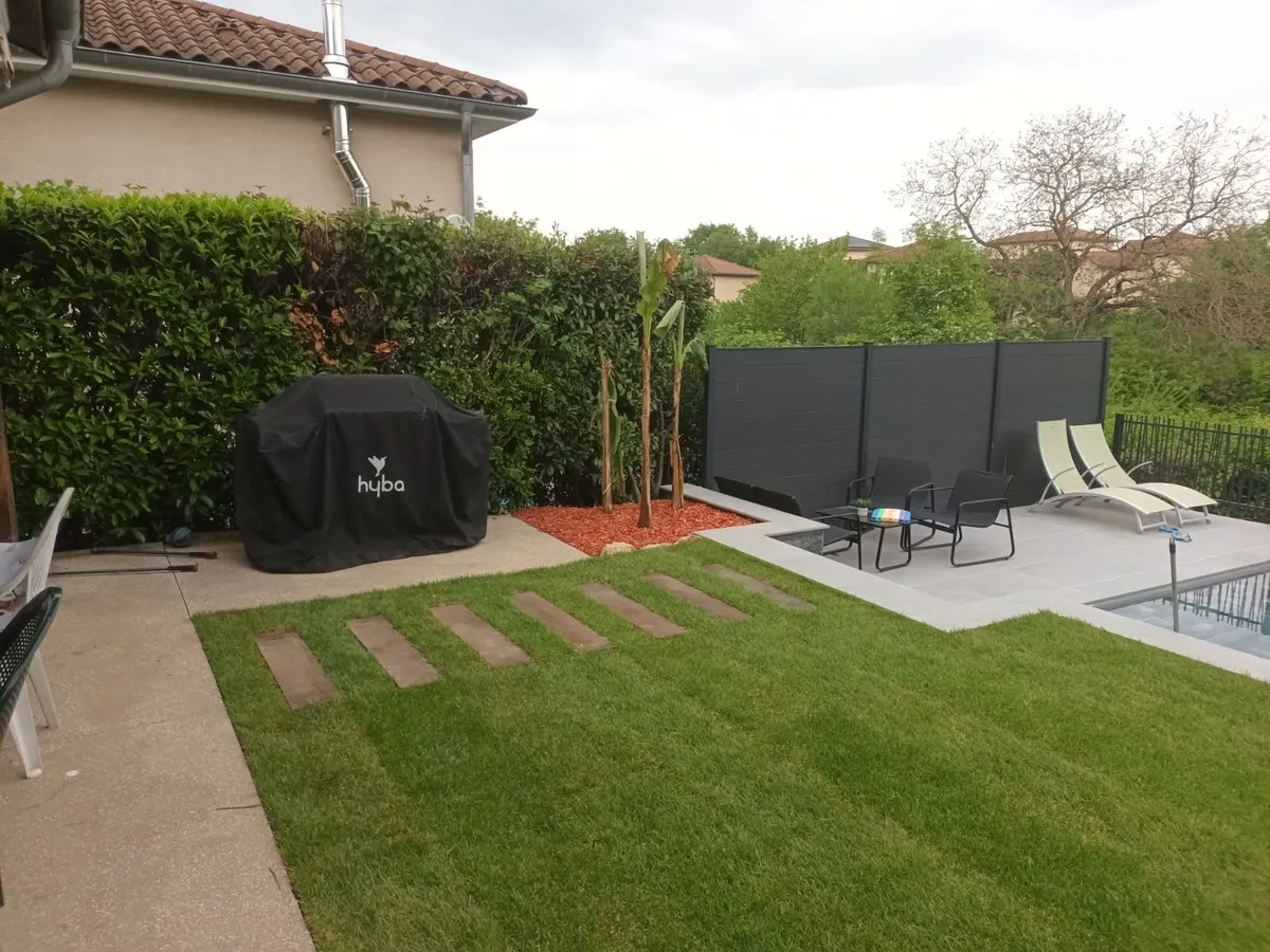 Terrasse dallée avec salon de jardin, pas japonais dans la pelouse, haie et clôture en fond