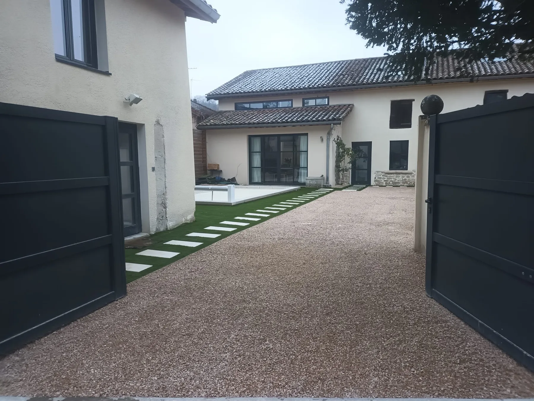 Cour en gravillon lavé avec pas japonais en dalles, portail et maison contemporaine
